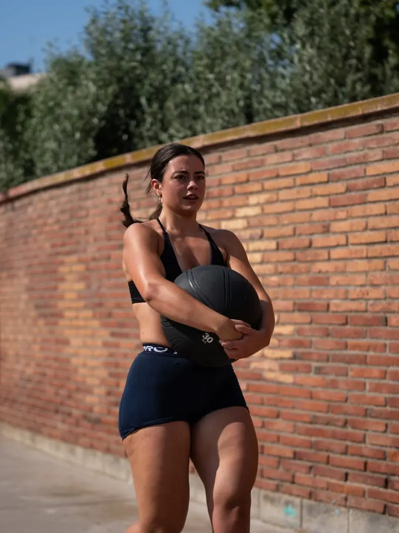 Atleta con un balón medicinal junto a un muro de ladrillo
